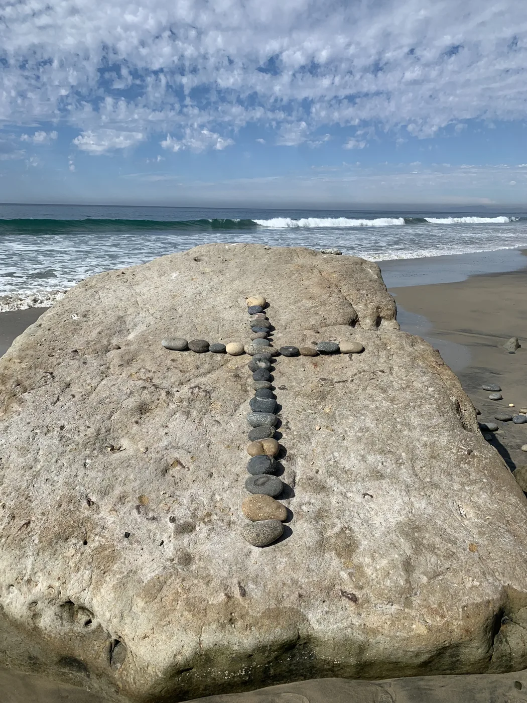 A cross made of stones arranged on a rock at the beach, with the ocean behind on the South Carolina coast